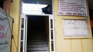 A hotel entrance with a staircase leading inside, a sign listing services like TV, cable, and internet, and a contact number (782) 82.355.75.