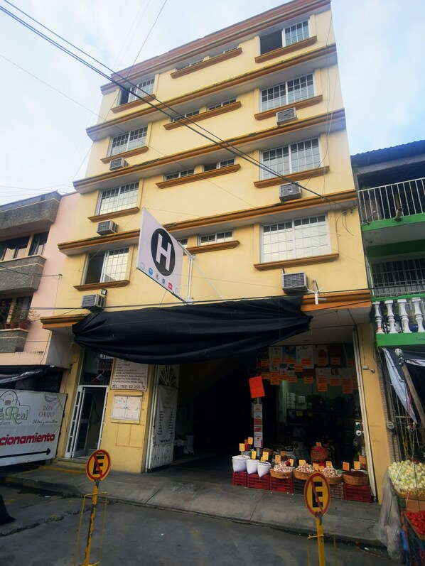 A multi-story building with a yellow facade, a sign indicating a hotel, and a storefront with produce displayed outside.