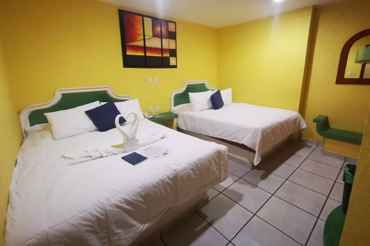A hotel room with two beds, each with white bedding and green headboards, a small bedside table with a lamp, and a wall-mounted painting.