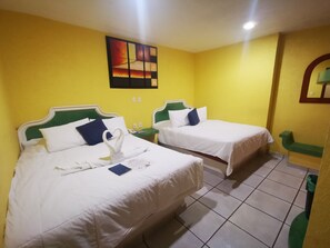A hotel room with two beds, each with white bedding and green headboards, a small bedside table with a lamp, and a wall-mounted painting.