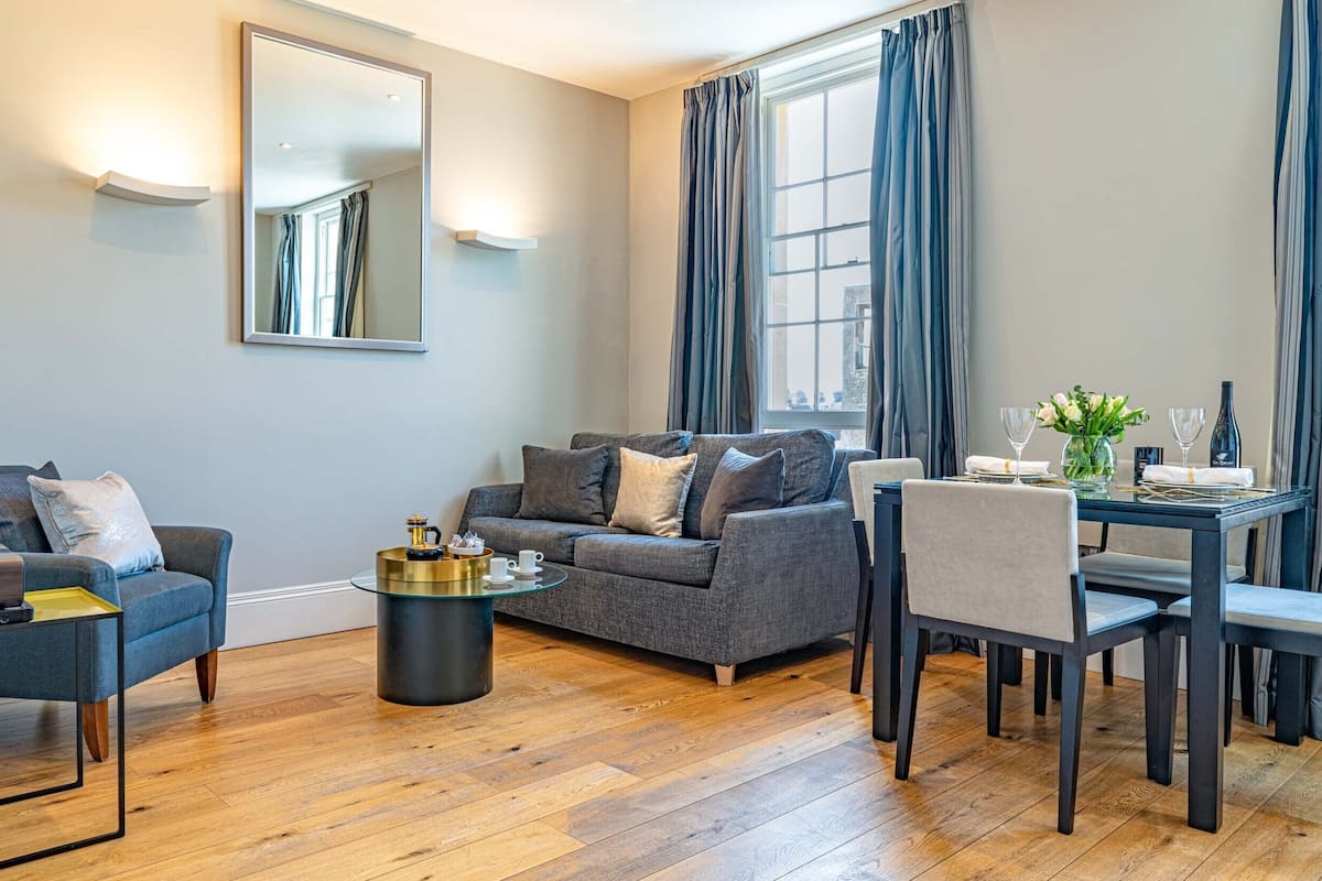 Un salon moderne avec un canapé gris, une table basse ronde et une table à manger dressée pour deux personnes.