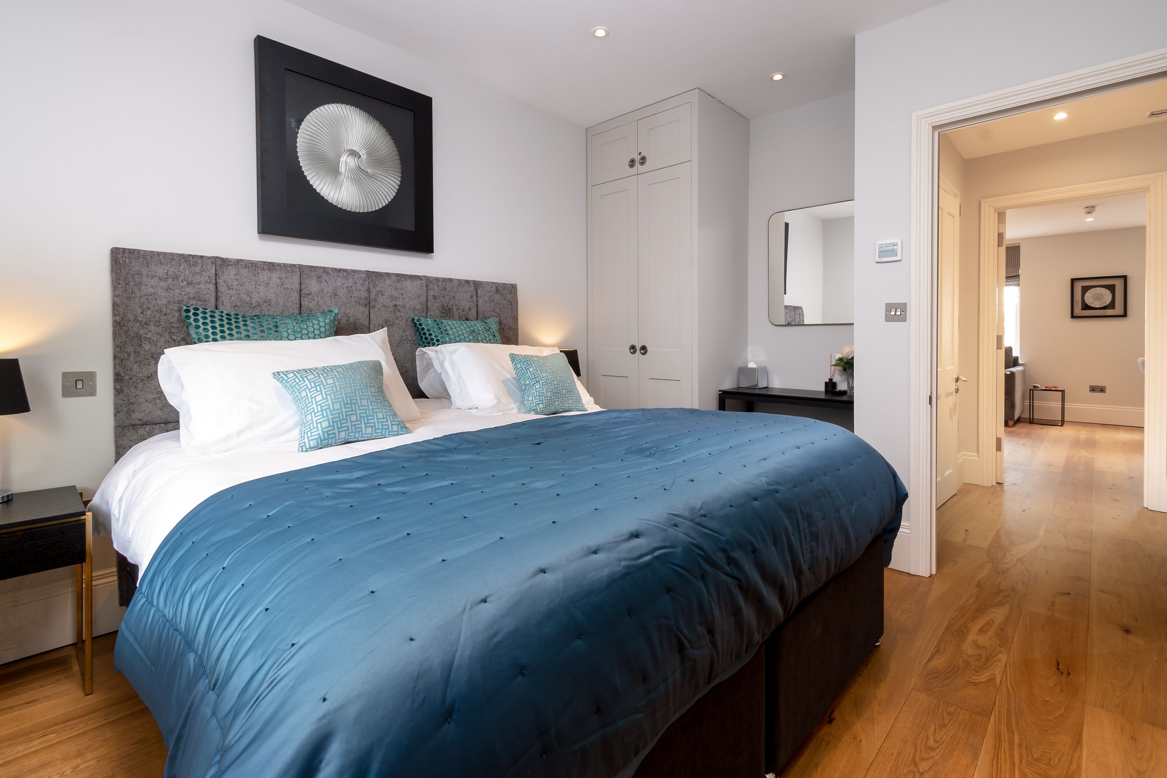 Een moderne slaapkamer met een groot bed, een grijze hoofdbord en een witte kledingkast.
