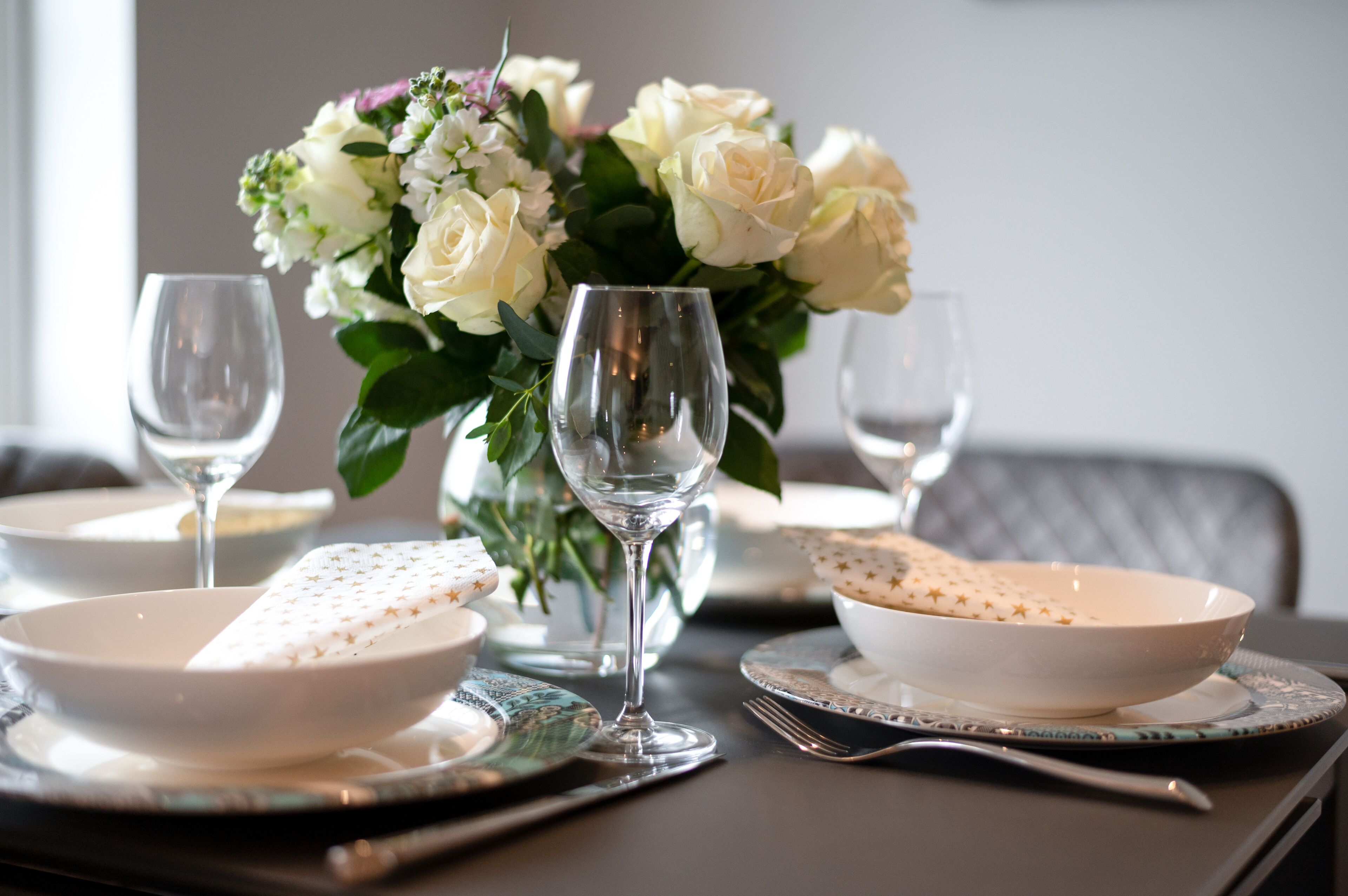 A dining table set with white plates, star-patterned napkins, and clear wine glasses.