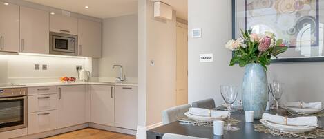 Een moderne keuken met witte kastjes, een magnetron en een eethoek met een tafel voor vier personen.