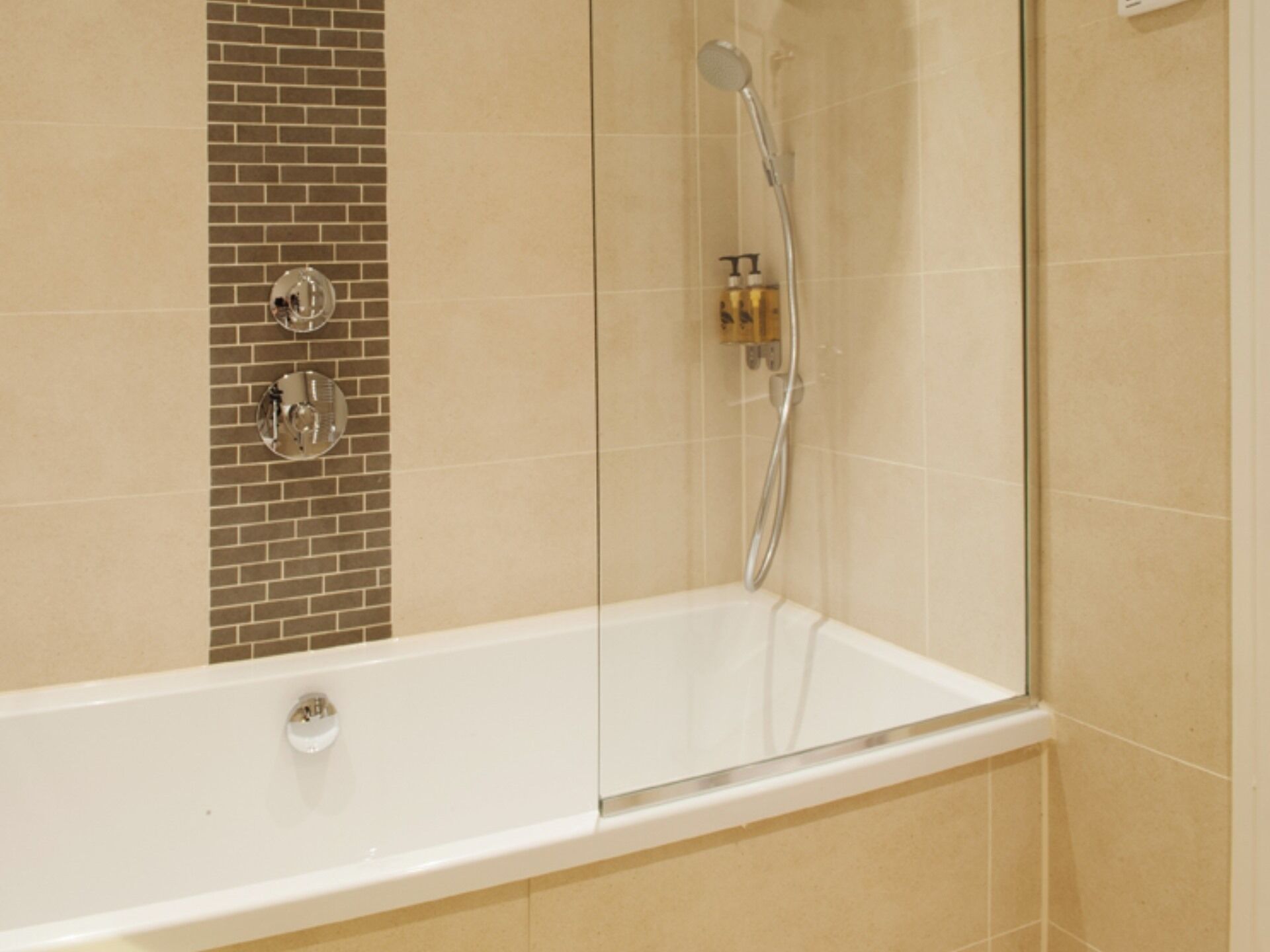 A modern bathroom with a glass-enclosed shower, a white bathtub, and a tiled wall with a brick pattern.