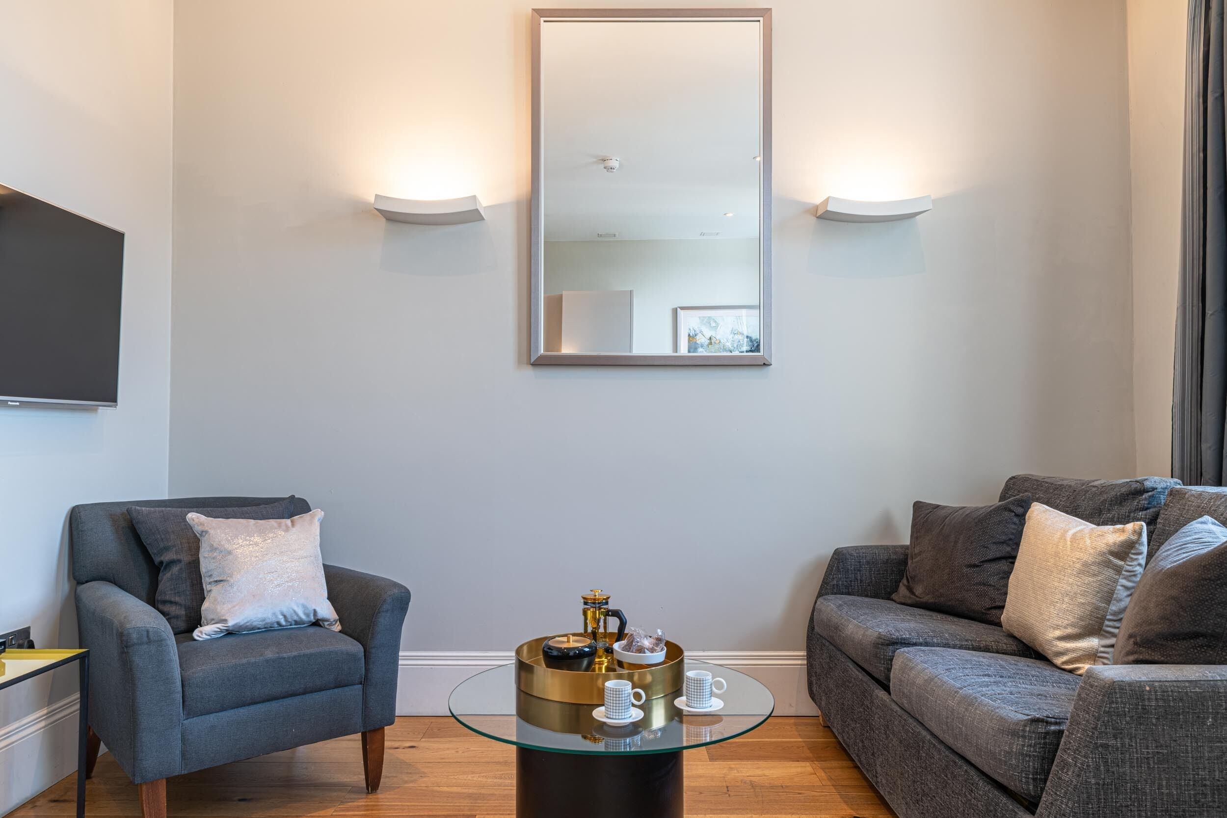 A modern living room with a grey sofa, a grey armchair, and a glass coffee table with a decorative item.