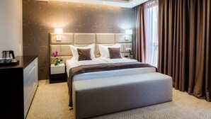 Habitación de hotel con una cama grande, una mesita de noche con lámpara, un aparador y un ventanal con cortinas.