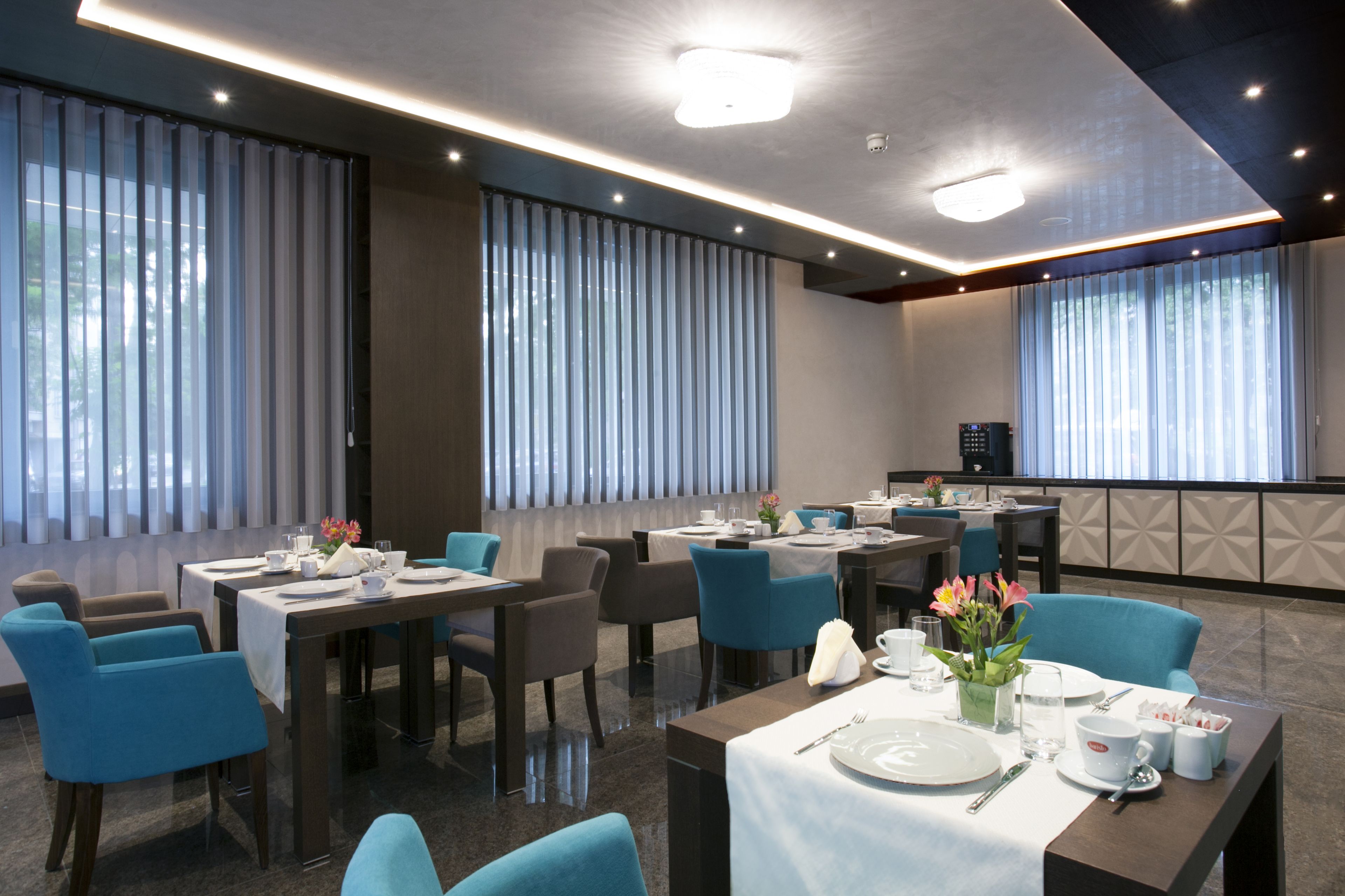 A modern dining area with tables set for four, blue chairs, and a kitchen in the background.