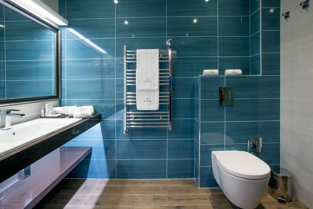 Une salle de bain moderne avec un grand miroir, un lavabo blanc, un porte-serviettes avec une serviette blanche, des toilettes et une poubelle.