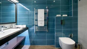 Une salle de bain moderne avec un grand miroir, un lavabo blanc, un porte-serviettes avec une serviette blanche, des toilettes et une poubelle.