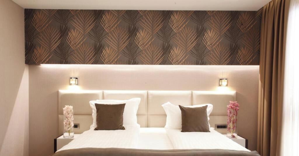 Un lit double avec deux oreillers, une table de chevet avec un vase, et un mur décoré d'un motif.
