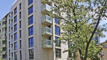 A multi-story hotel with balconies, a parking area, and a tree in the foreground.