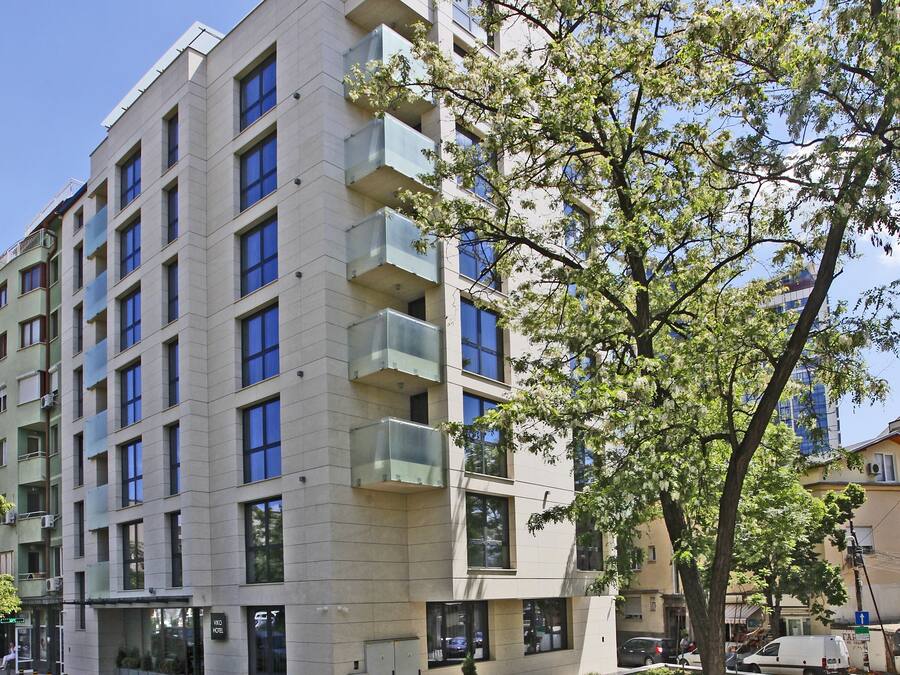 A multi-story hotel with balconies, a parking area, and a tree in the foreground.
