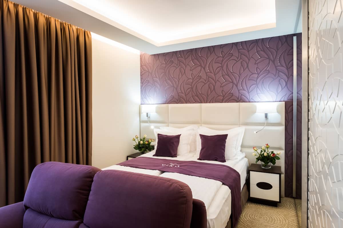 Een moderne hotelkamer met een groot bed, een nachtkastje met een bloevas en een paarse fauteuil.