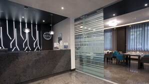 Un área de recepción moderna con mostrador de mármol, lámparas decorativas y un separador de vidrio con el nombre "WILCO".