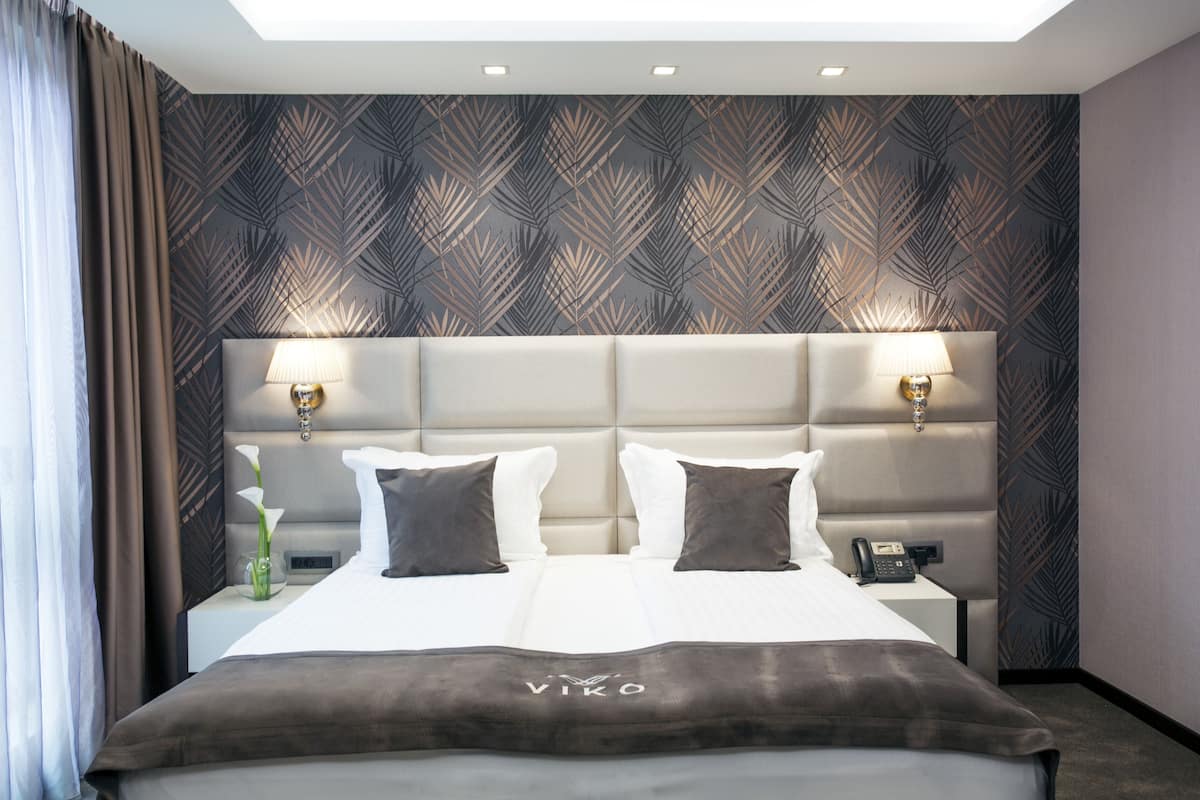 Een moderne hotelkamer met een groot bed, twee bedlampjes, een nachtkastje en behang met een patroon.