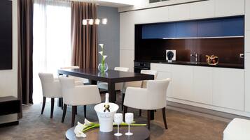 A modern dining area with a dark wooden table, white chairs, a vase with flowers, and a bottle of champagne.
