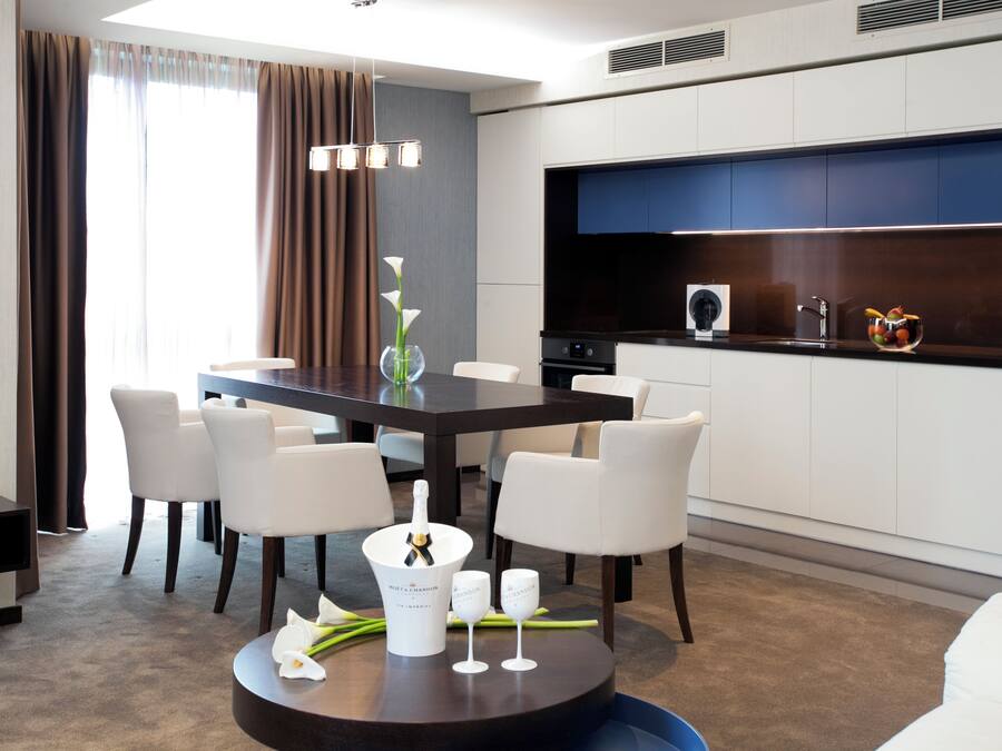 A modern dining area with a dark wooden table, white chairs, a vase with flowers, and a bottle of champagne.