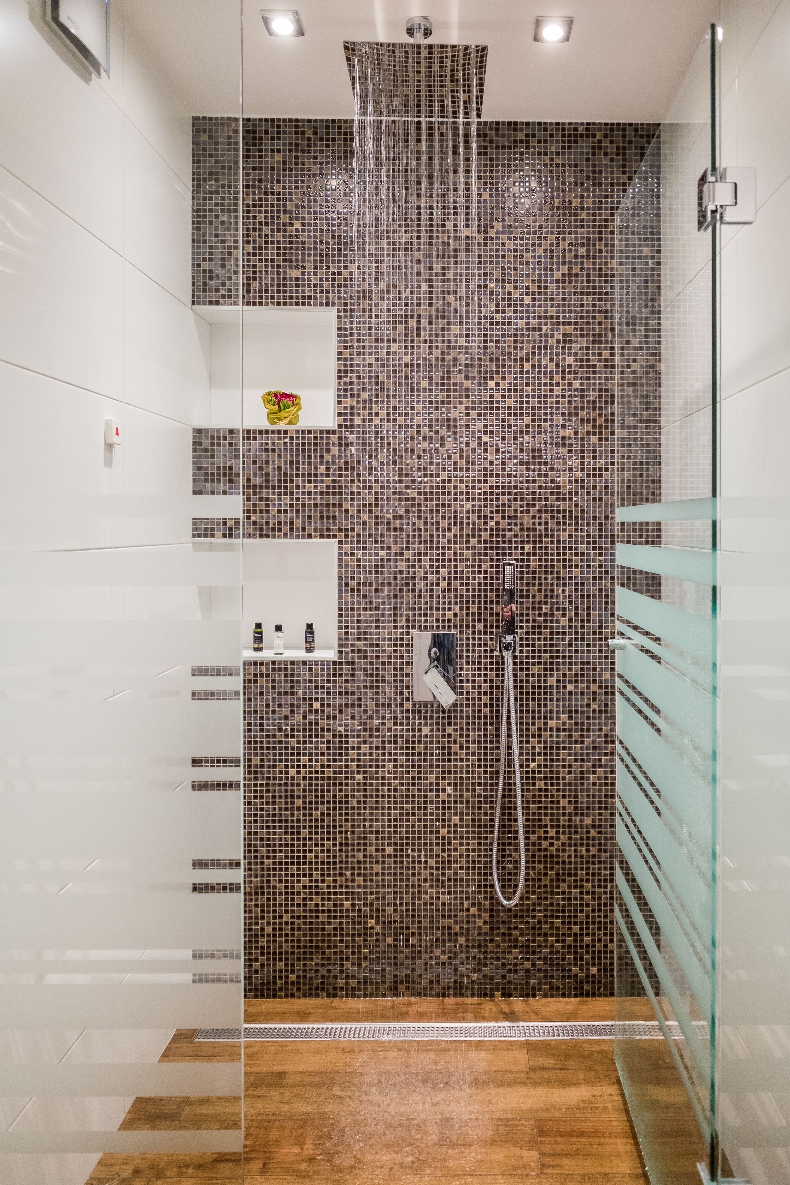 A modern shower with mosaic tiles, a glass enclosure, and a wooden floor.