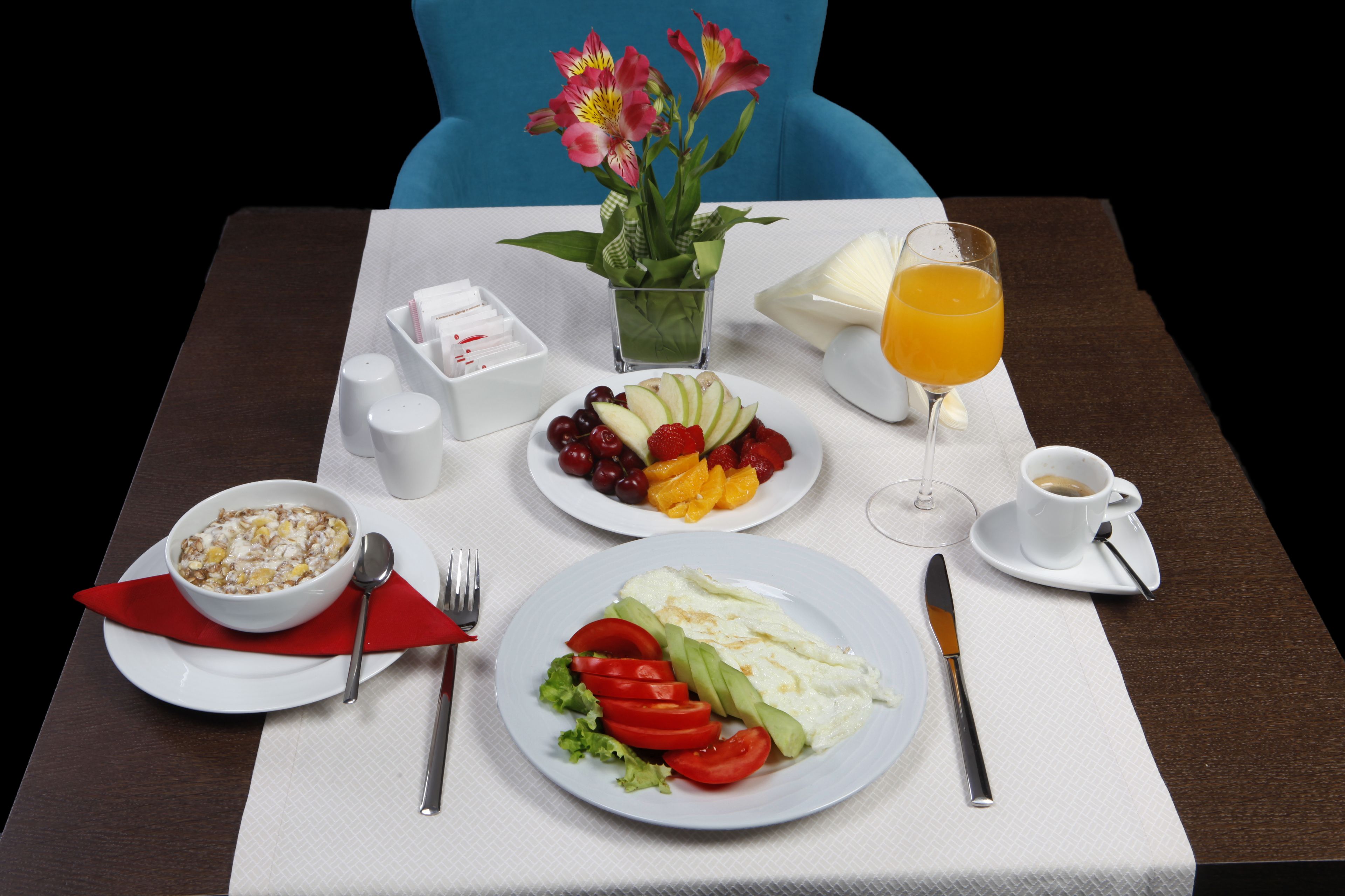 Une table mise pour le petit-déjeuner, avec un bol de céréales, une assiette de fruits, un verre de jus d’orange et une tasse de café.