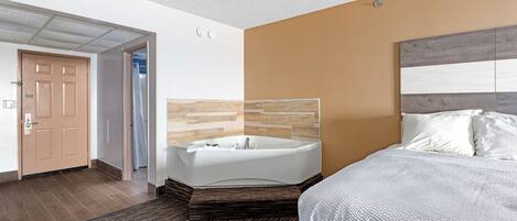 A hotel room with a large bed, a wooden headboard, a bathtub, and a carpeted floor.