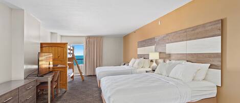 A hotel room with two beds, a desk, and a view of the ocean.