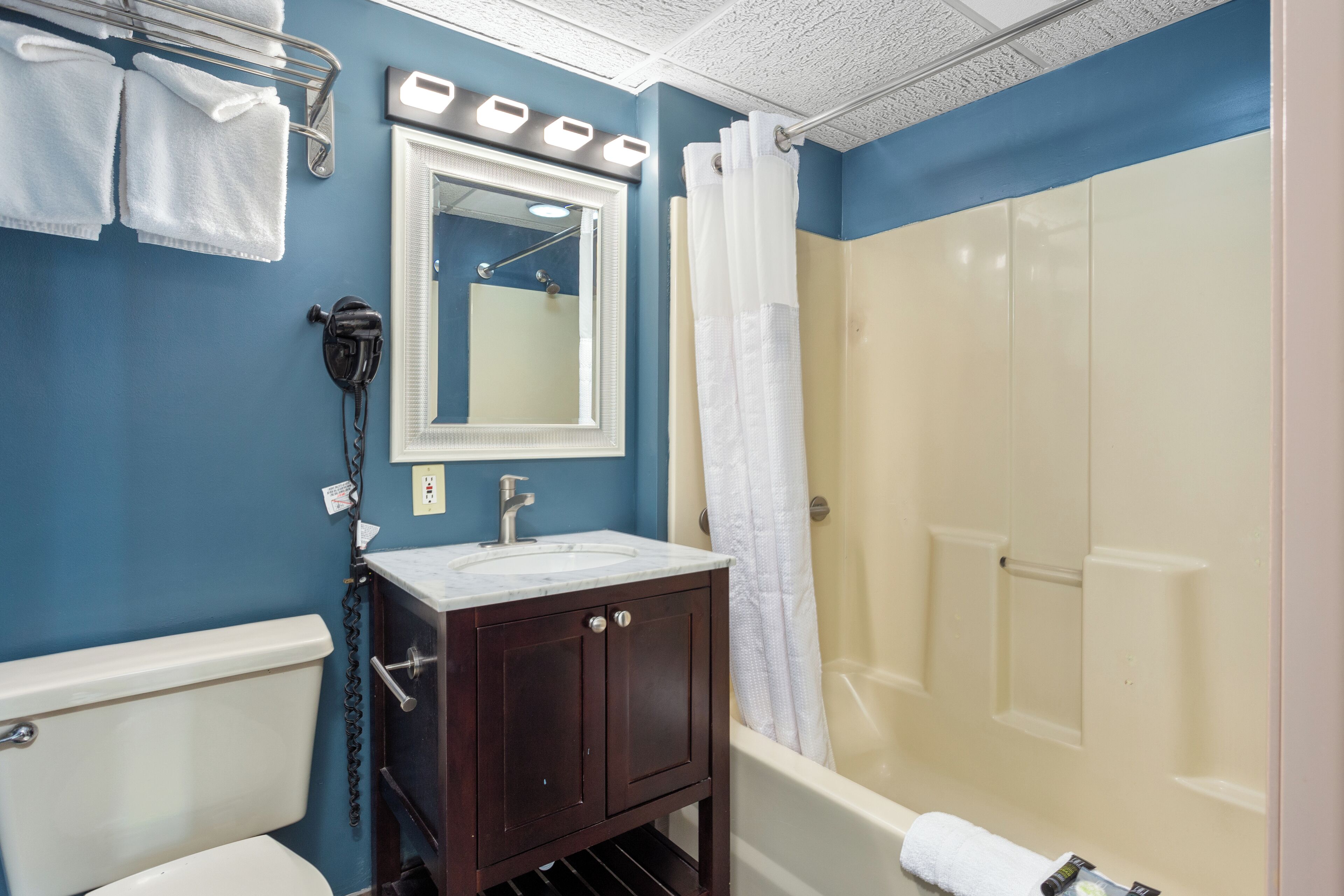 A bathroom with a blue wall, a white sink, a dark wooden vanity, a white toilet, a white shower curtain, and a white towel on the floor.