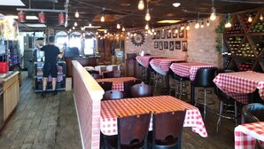 A restaurant interior with brick walls, checkered tablecloths, hanging light bulbs, and a bar area. - Americana Motor Inn (Ocean City)