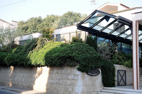 A modern building with a glass facade, a stone wall with greenery, and a sign indicating a hotel and restaurant. - Hotel & Restaurant Milan (Pula)