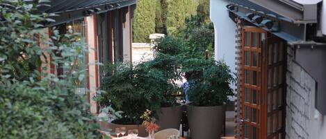 A covered outdoor area with potted plants, a tiled floor, and a wooden door.