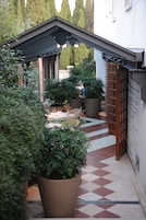 A covered outdoor area with potted plants, a tiled floor, and a wooden door.