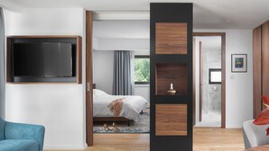 A modern hotel room with a large flat-screen TV, a bed with a gray blanket, a blue sofa, and a wooden accent wall. - Hotel & Restaurant Milan (Pula)