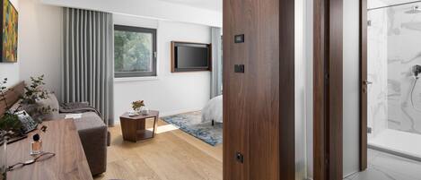 Una sala de estar moderna con piso de madera, un sofá gris, una mesita con un florero y un televisor montado en la pared.