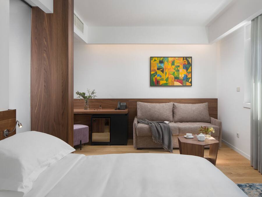 Una habitación de hotel moderna con una cama, un escritorio, un sofá y una pequeña mesa con tetera.