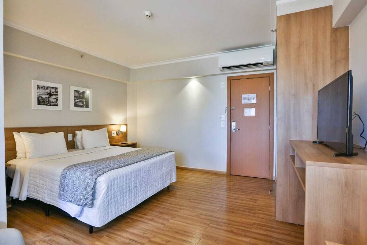 Una habitación de hotel con cama, mesitas de noche, televisor y aire acondicionado.