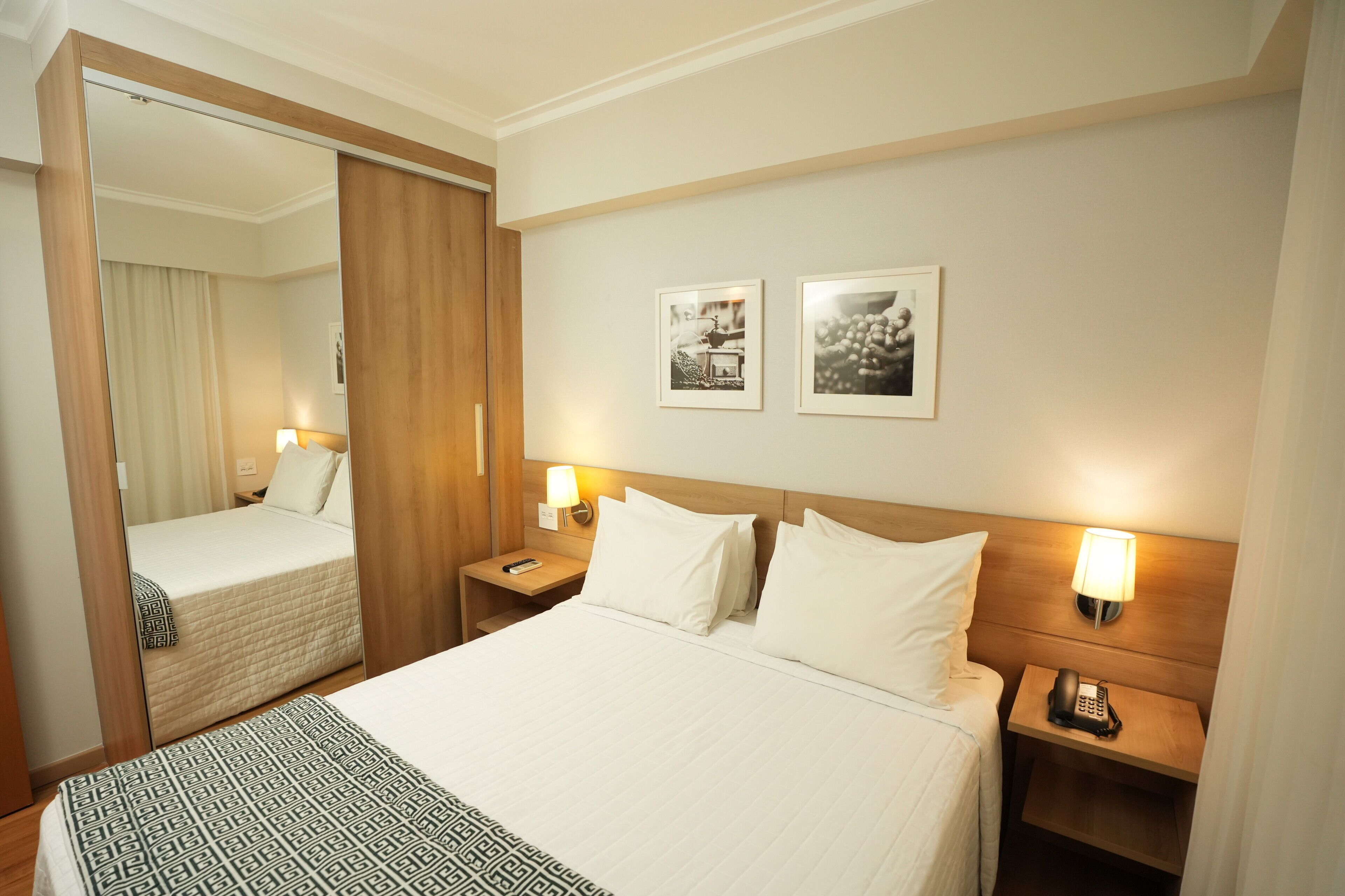 Una habitación de hotel con cama, mesitas de noche, un espejo y dos cuadros en la pared.