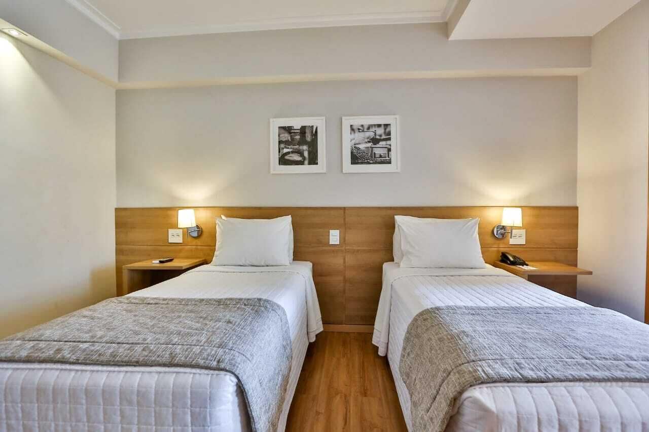 A hotel room with two single beds, wooden headboards, bedside lamps, and two framed pictures on the wall.