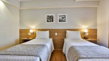 A hotel room with two single beds, wooden headboards, bedside lamps, and two framed pictures on the wall.