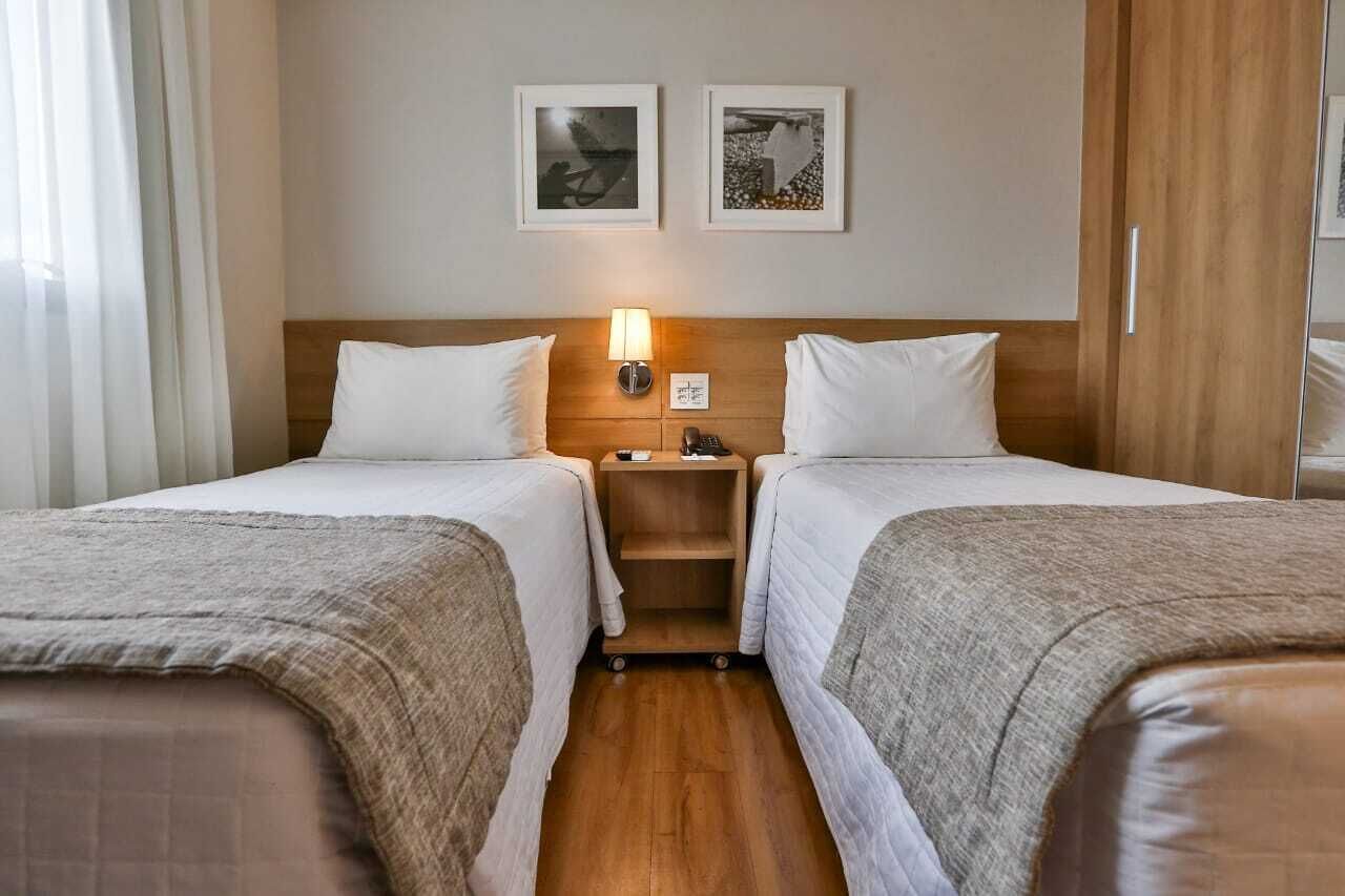 A hotel room with two beds, a nightstand, a lamp, and two framed pictures on the wall.