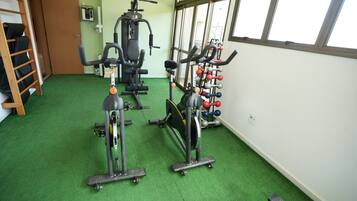 Ein Fitnessraum mit Trainingsgeräten, grünem Teppich und großen Fenstern.