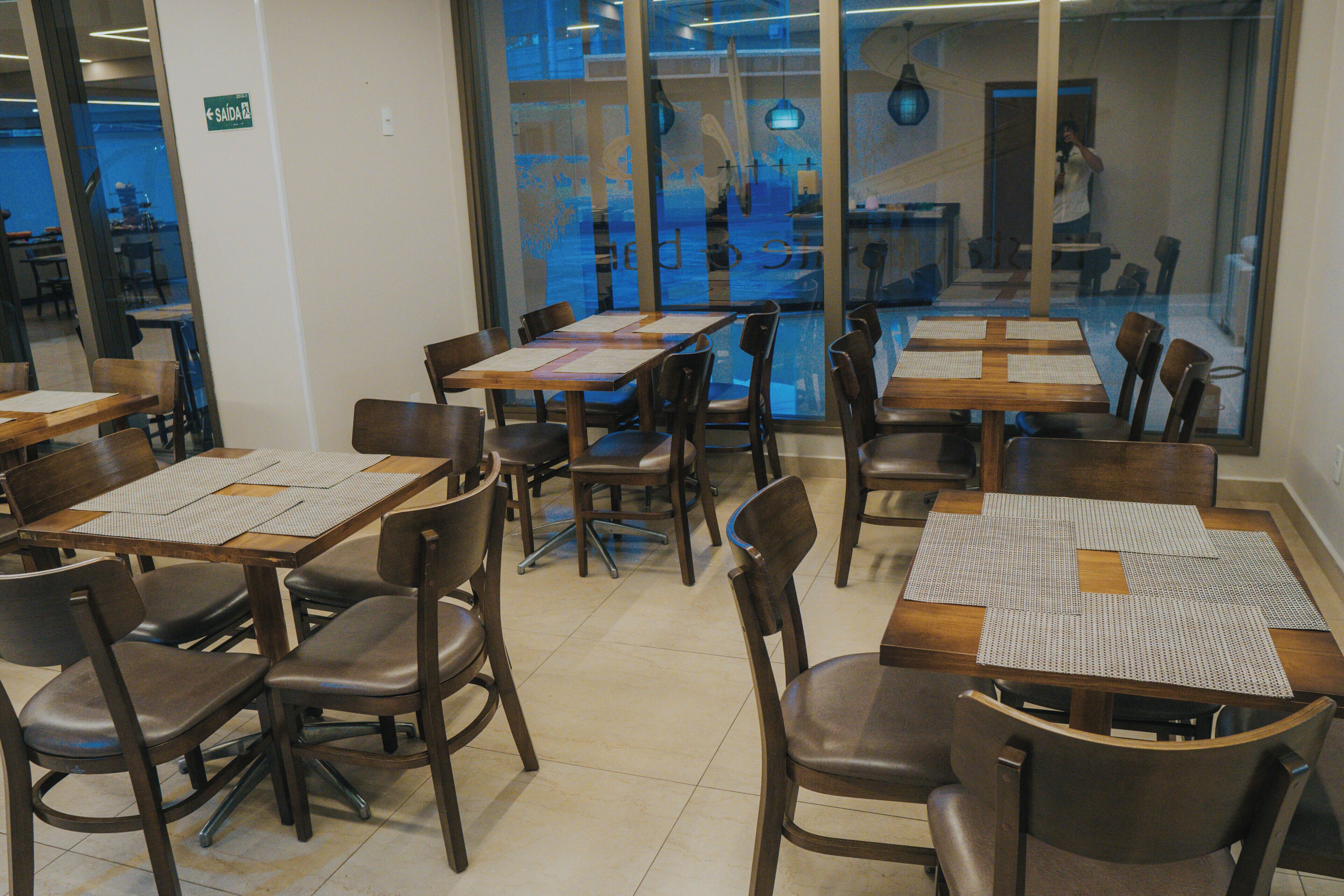 Interior de restaurante con varias mesas y sillas, piso de baldosas y vista a través del muro de cristal.