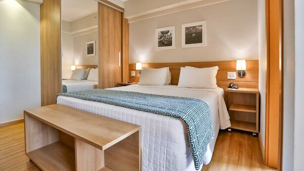 A hotel room with a bed, bedside tables, a bench, and a mirror. -  Matiz Vilaboim Ribeirão Preto (Ribeirão Preto)