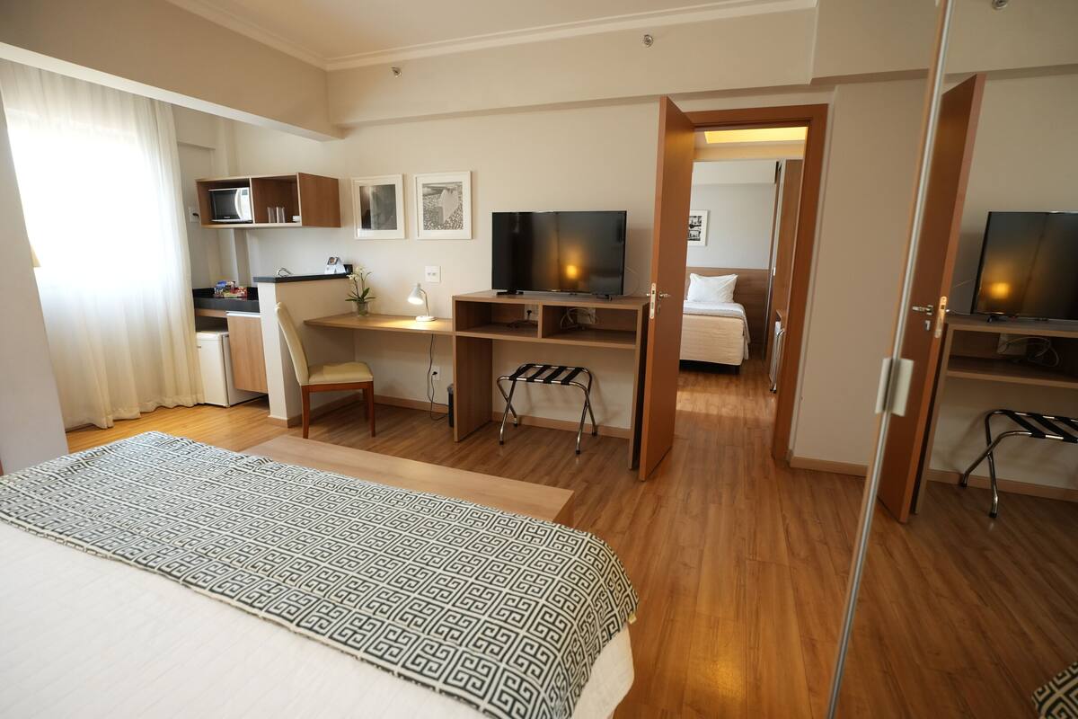 Una habitación de hotel con una cama, un escritorio, un televisor y una kitchenette.