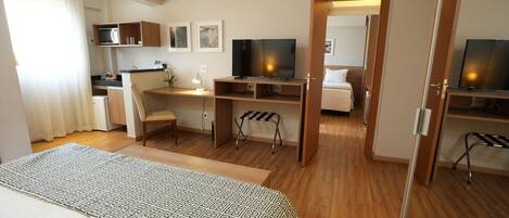 Una habitación de hotel con una cama, un escritorio, un televisor y una kitchenette.
