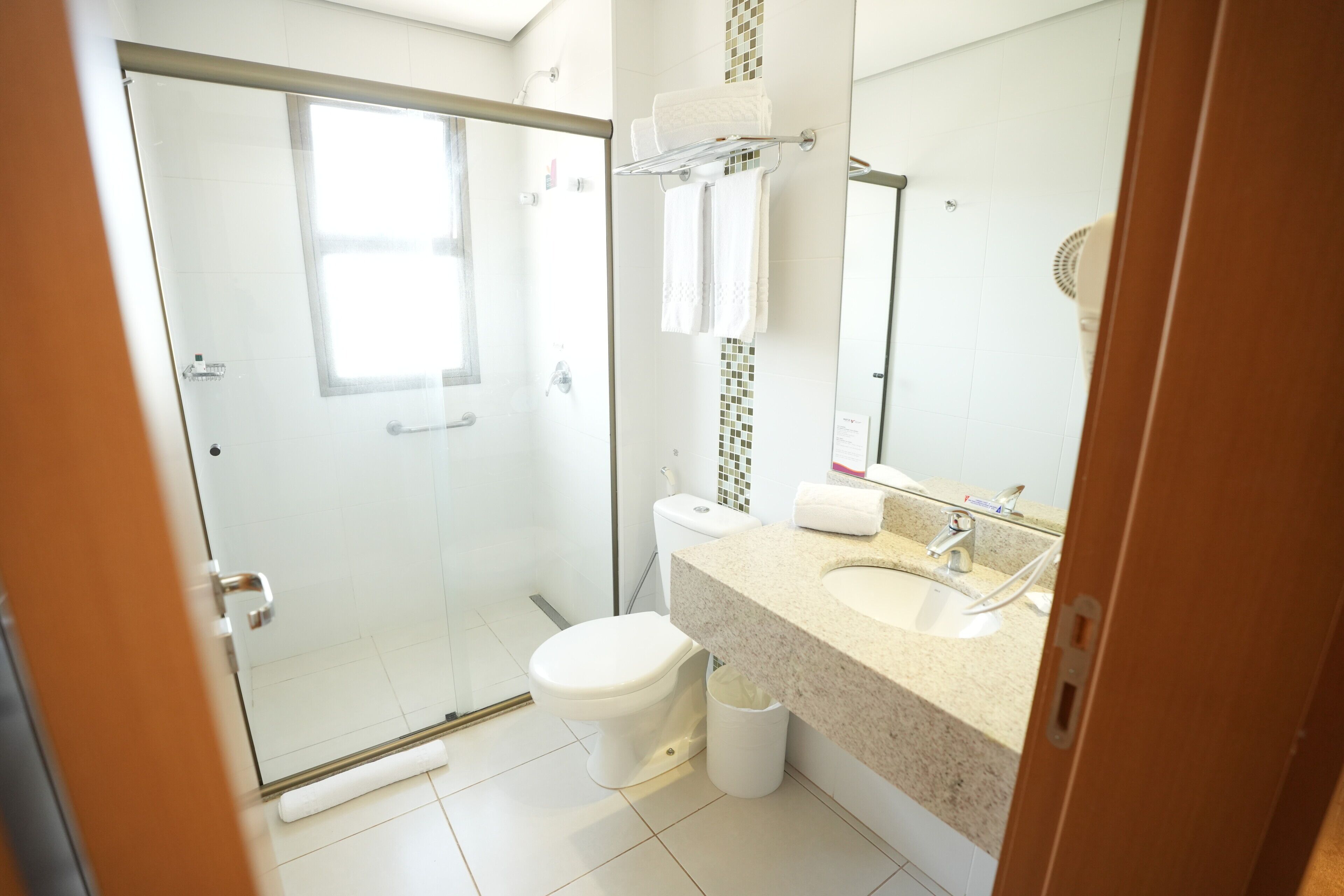 A bathroom with a glass shower enclosure, a toilet, a sink with a mirror, and a towel rack.