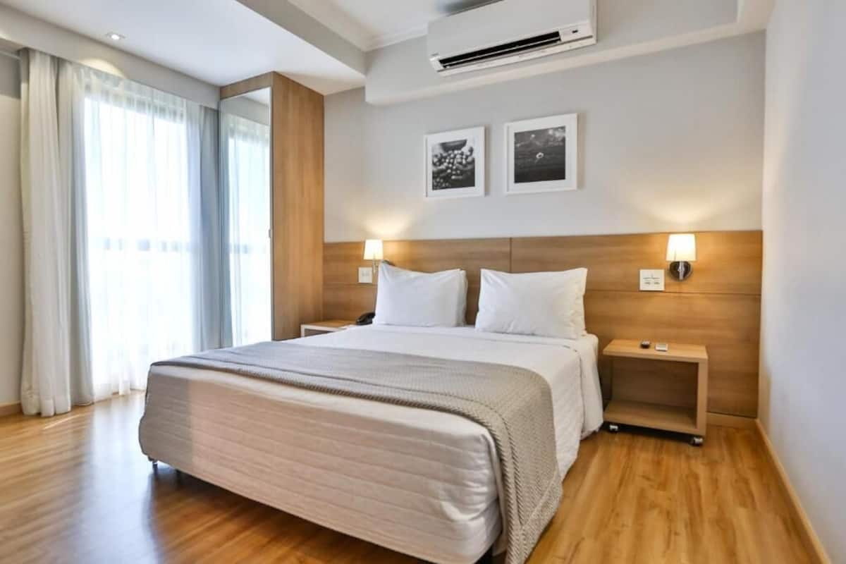Una habitación de hotel moderna con una cama grande, cabecera de madera, lámparas de noche y vistas a la ciudad por la ventana.