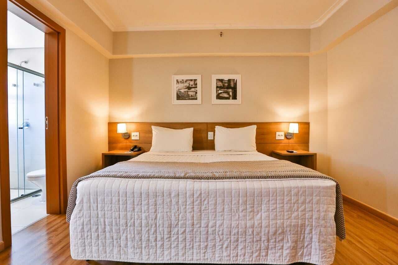 A hotel room with a large bed, two bedside tables with lamps, a wooden headboard, and two framed pictures on the wall.