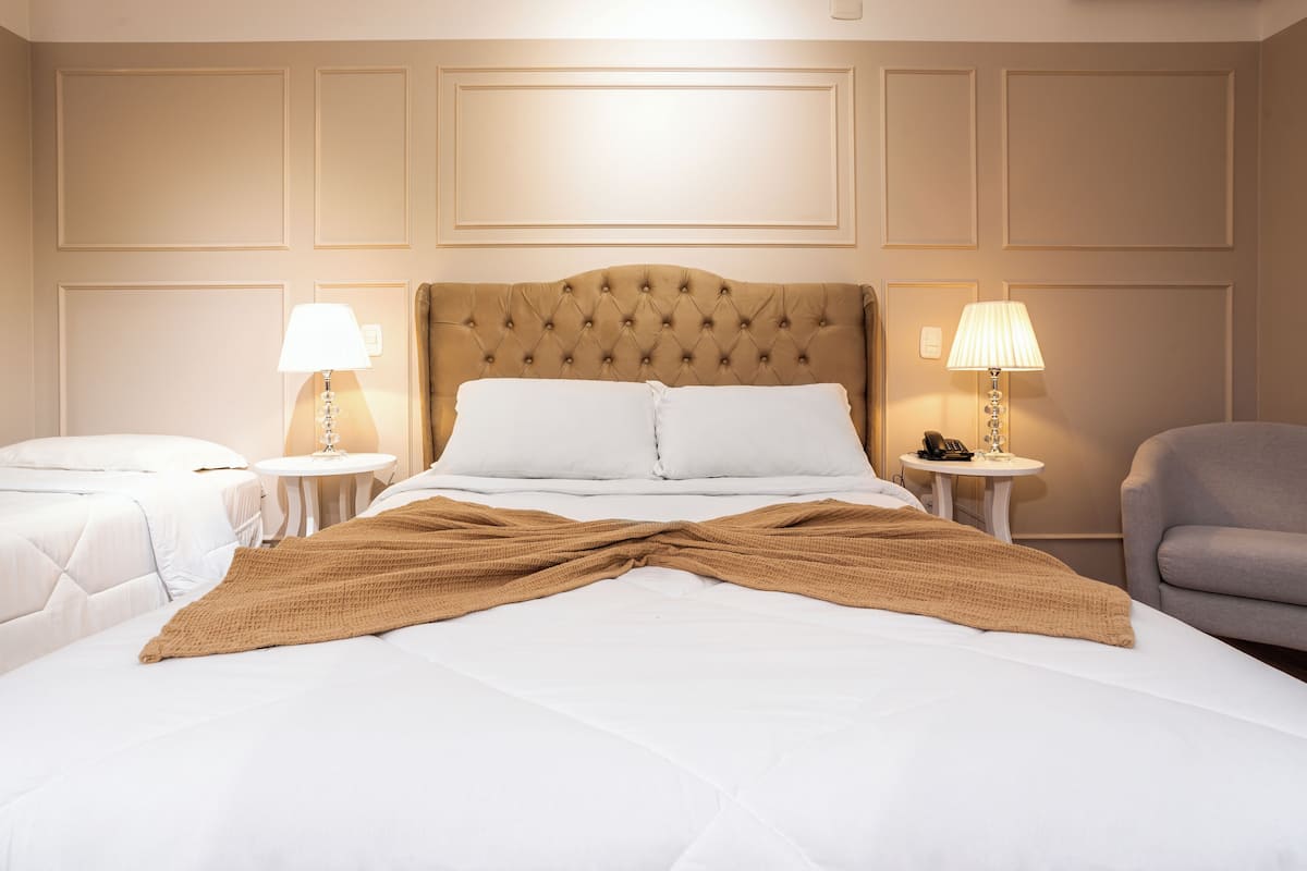 Habitación de hotel con una cama grande, dos mesitas de noche con lámparas, una silla y un cabecero decorativo.