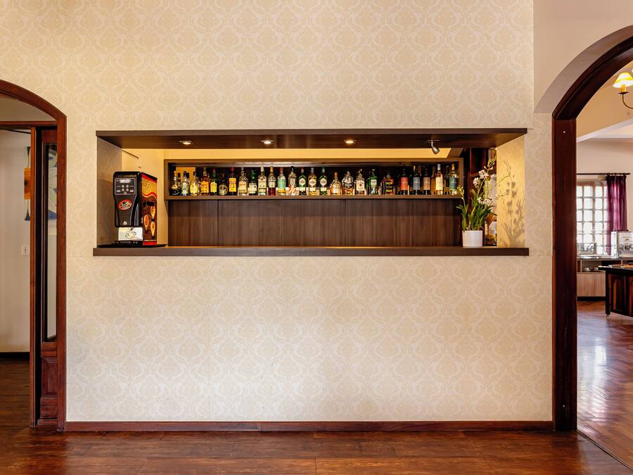 Zona de bar con papel tapiz estampado, suelo de madera y varios botellas en estanterías.