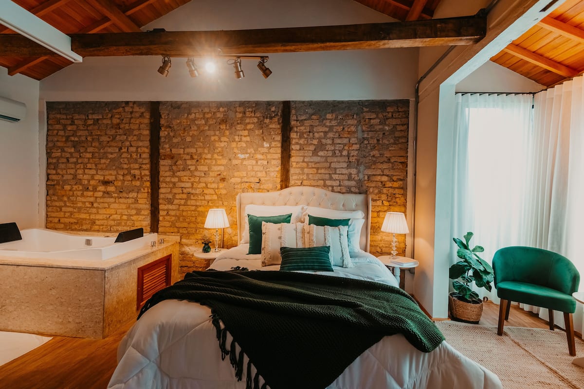Un dormitorio con pared de ladrillo, una cama grande, un sillón verde y una bañera.